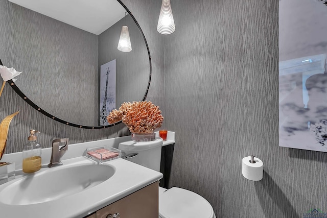 half bath featuring vanity, wallpapered walls, and toilet
