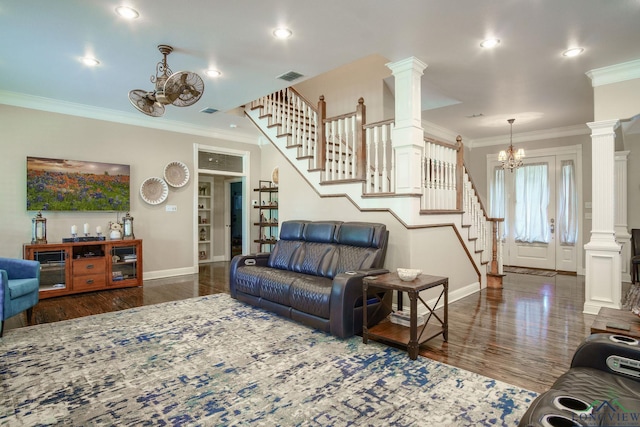 living room featuring ornate columns, dark wood-type flooring, ornamental molding, and an inviting chandelier