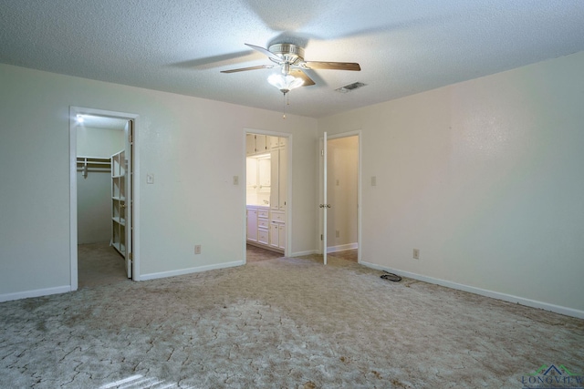 unfurnished bedroom with light carpet, a walk in closet, a closet, and ceiling fan