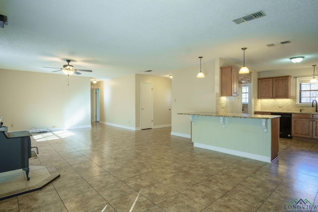 kitchen with a kitchen breakfast bar, light stone counters, ceiling fan, black dishwasher, and hanging light fixtures