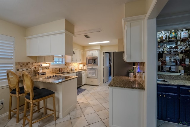 kitchen with backsplash, white cabinets, dark stone countertops, kitchen peninsula, and stainless steel appliances