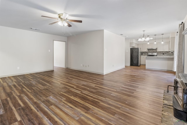 unfurnished living room with dark wood-type flooring and ceiling fan with notable chandelier