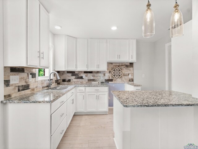 kitchen with decorative backsplash, white cabinetry, a sink, light wood-type flooring, and light stone counters