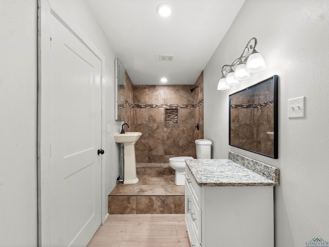 full bathroom featuring toilet, a sink, visible vents, tiled shower, and wood finished floors
