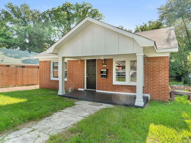 view of front of house with a front yard, covered porch, fence, board and batten siding, and brick siding