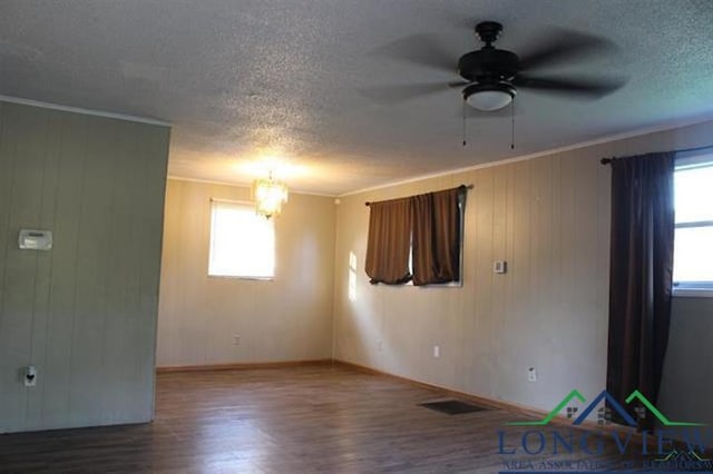 spare room featuring wooden walls, ceiling fan with notable chandelier, hardwood / wood-style flooring, and ornamental molding