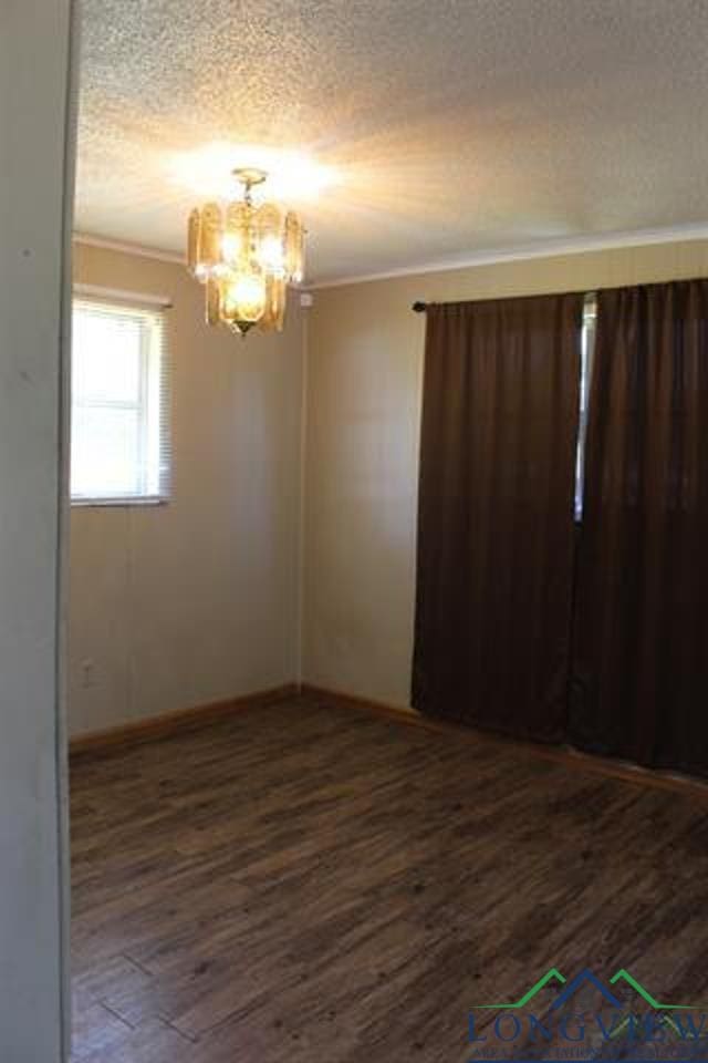 unfurnished room featuring a textured ceiling, ornamental molding, dark hardwood / wood-style floors, and a notable chandelier