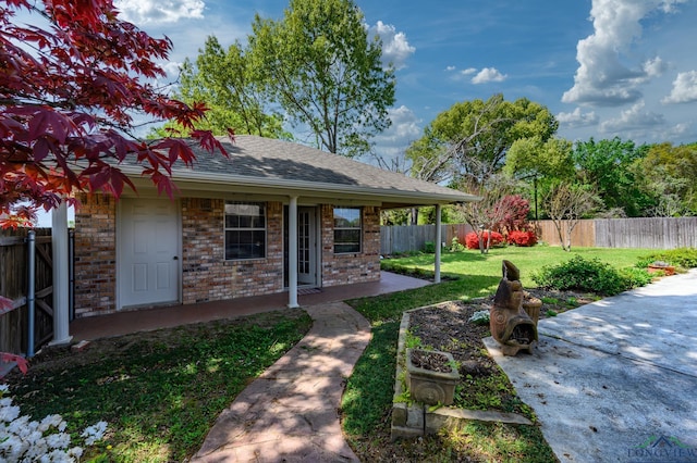 view of front of home with a shingled roof, a fenced backyard, a front yard, and brick siding