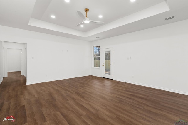 spare room with a tray ceiling, ceiling fan, and dark wood-type flooring