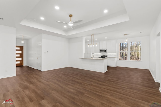 unfurnished living room with a tray ceiling, ceiling fan, dark hardwood / wood-style flooring, and sink