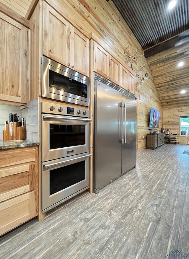 kitchen featuring light brown cabinetry, wood walls, vaulted ceiling with beams, built in appliances, and light hardwood / wood-style floors