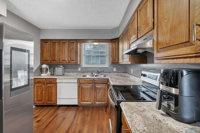 kitchen featuring sink, dark wood-type flooring, light stone counters, a textured ceiling, and stainless steel appliances