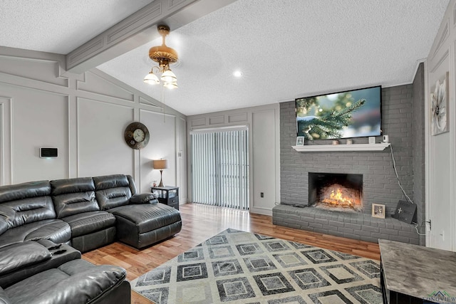 living room with wood-type flooring, lofted ceiling with beams, a textured ceiling, and a brick fireplace