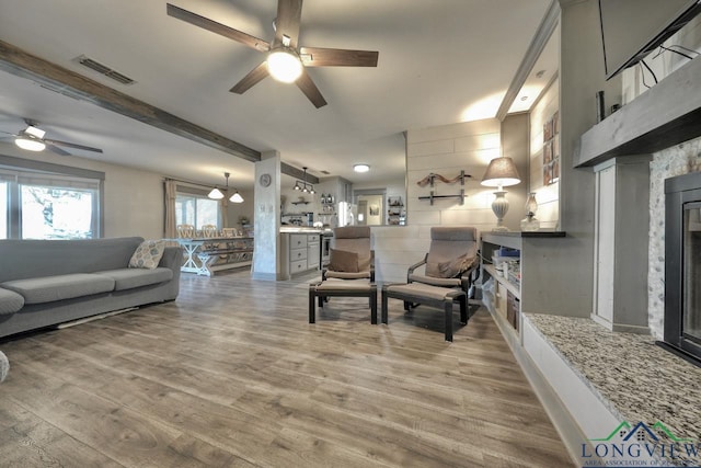 living area featuring a fireplace, wood finished floors, visible vents, and ceiling fan