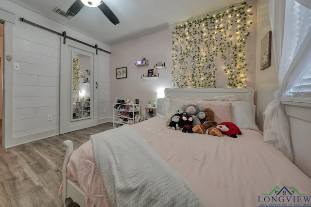 bedroom featuring visible vents, ceiling fan, a barn door, ornamental molding, and wood finished floors