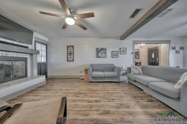 living area with visible vents, beam ceiling, wood finished floors, a glass covered fireplace, and ceiling fan