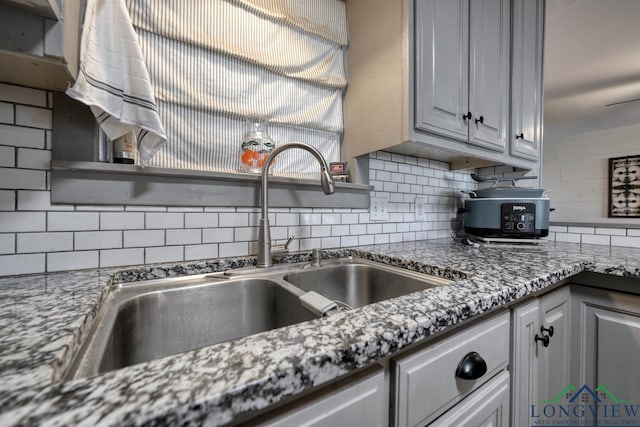 kitchen featuring tasteful backsplash, stone countertops, and a sink