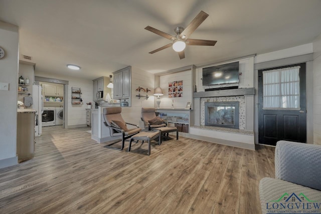 living area featuring a ceiling fan, visible vents, light wood finished floors, washing machine and dryer, and a large fireplace