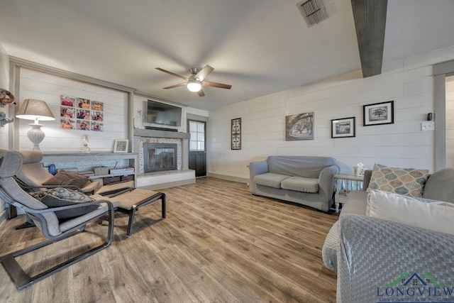 living area featuring a glass covered fireplace, wood finished floors, a ceiling fan, and visible vents