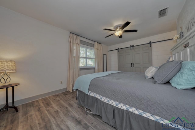 bedroom featuring visible vents, a ceiling fan, wood finished floors, a barn door, and baseboards