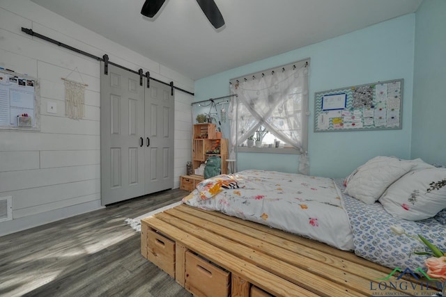 bedroom featuring wood finished floors, ceiling fan, a closet, wood walls, and a barn door