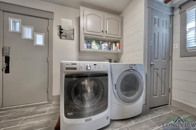 laundry room featuring cabinet space, wooden walls, wood tiled floor, and washer and clothes dryer