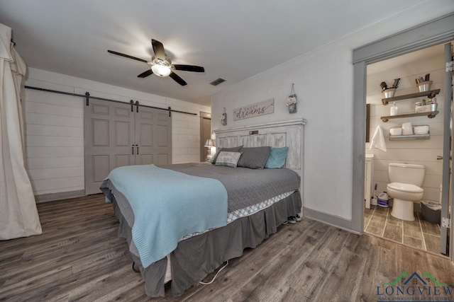 bedroom featuring a barn door, wood finished floors, visible vents, and ceiling fan