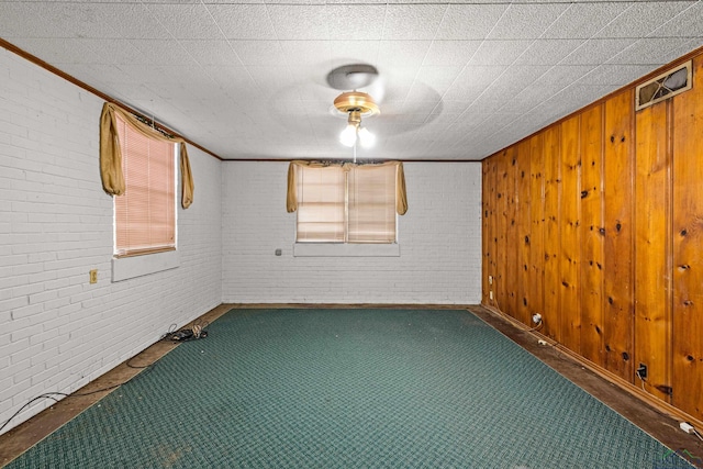 unfurnished room with wood walls, ornamental molding, and brick wall