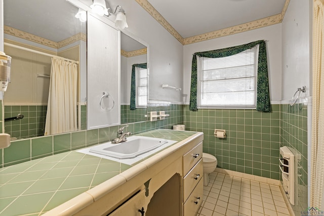 bathroom with tile patterned floors, heating unit, toilet, vanity, and tile walls