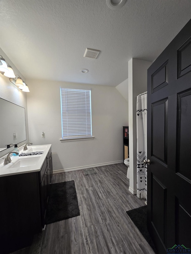 203 W Gay Ave, Gladewater, TX 75647 - full bath with toilet, vanity, wood finished floors, a textured ceiling, and baseboards