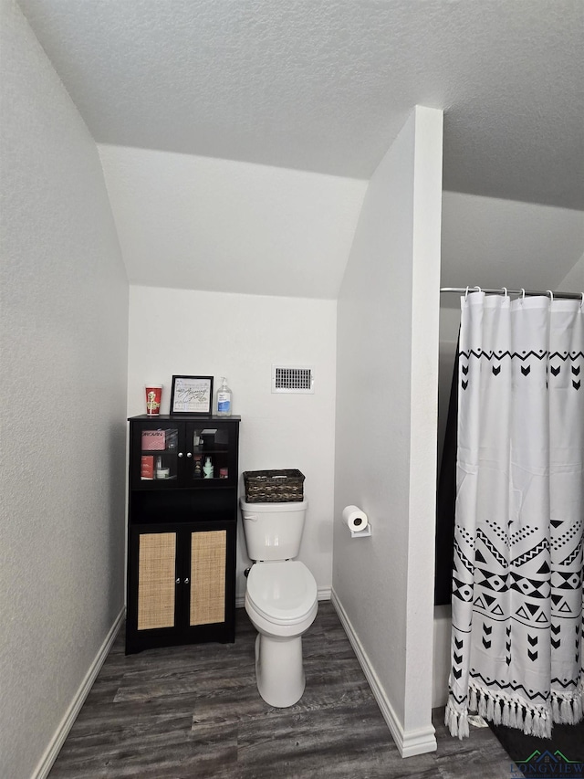 203 W Gay Ave, Gladewater, TX 75647 - full bath with vaulted ceiling, baseboards, toilet, wood finished floors, and a textured ceiling
