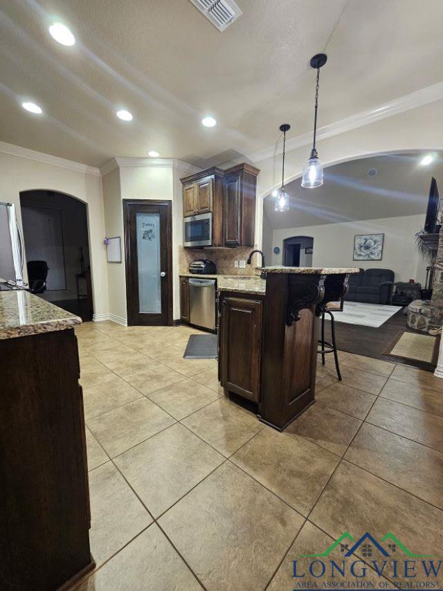 240 Cedar Ridge Rd, Longview, TX 75602 - kitchen with crown molding, appliances with stainless steel finishes, a kitchen breakfast bar, light stone countertops, and backsplash