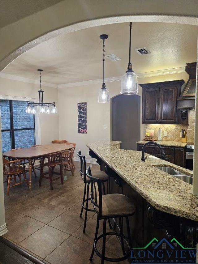 240 Cedar Ridge Rd, Longview, TX 75602 - kitchen featuring a sink, decorative backsplash, dark brown cabinets, ornamental molding, and light stone countertops