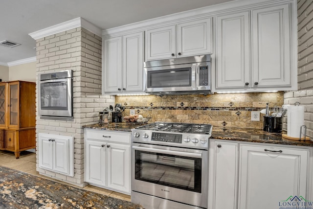 kitchen featuring white cabinets, ornamental molding, stainless steel appliances, and dark stone counters