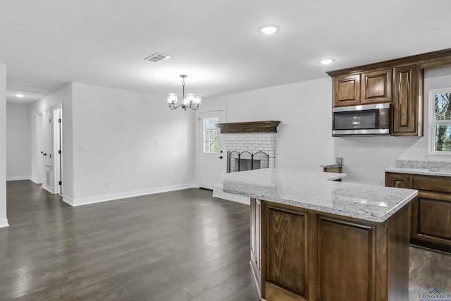 kitchen featuring a center island, hanging light fixtures, a brick fireplace, light stone countertops, and a notable chandelier