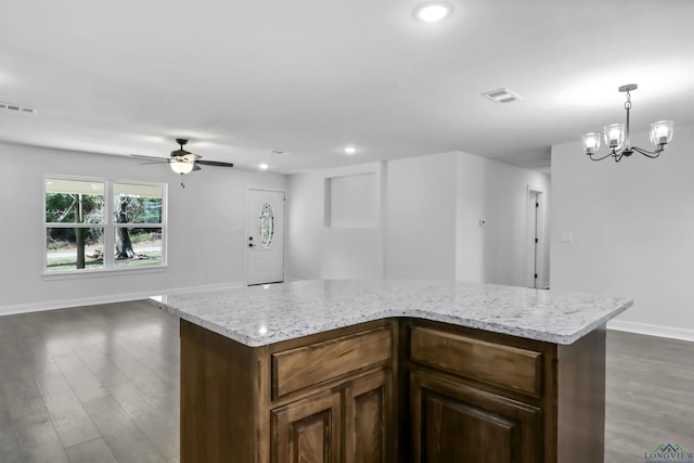 kitchen with a center island, dark wood-type flooring, ceiling fan with notable chandelier, hanging light fixtures, and light stone counters