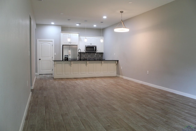 kitchen with backsplash, stainless steel appliances, decorative light fixtures, white cabinets, and hardwood / wood-style floors