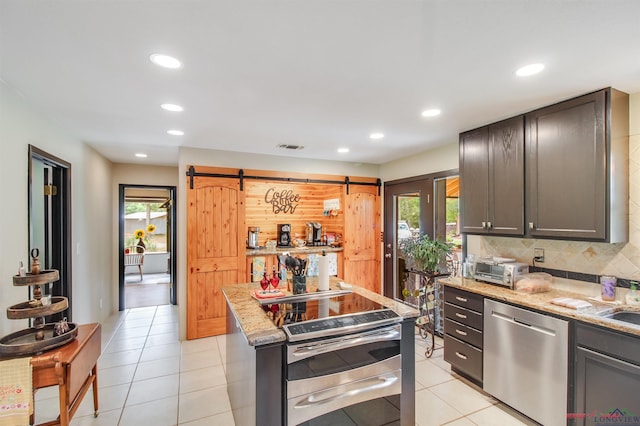 kitchen featuring a barn door, light stone counters, a healthy amount of sunlight, and appliances with stainless steel finishes