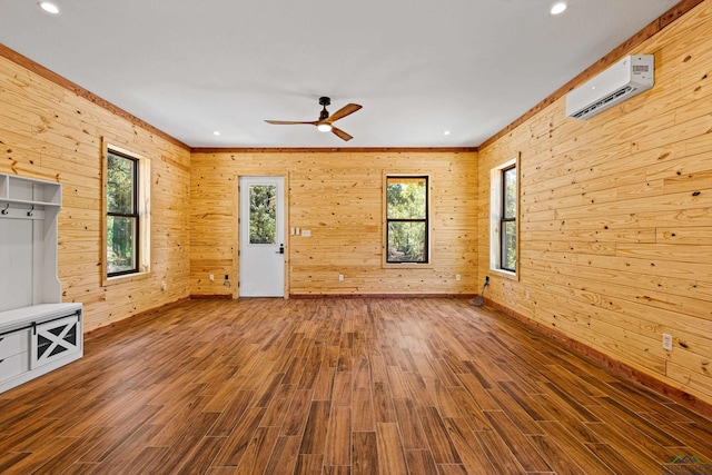 unfurnished living room featuring hardwood / wood-style flooring, an AC wall unit, ceiling fan, and wooden walls