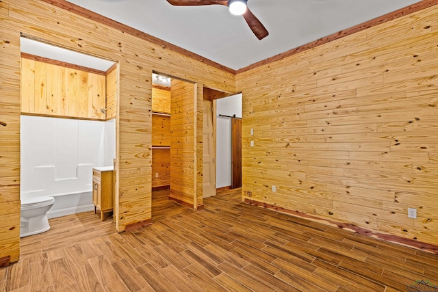 unfurnished bedroom featuring ensuite bathroom, ceiling fan, and wooden walls