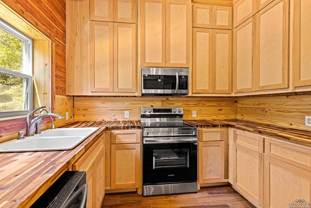 kitchen with sink, wood counters, wooden walls, light brown cabinetry, and appliances with stainless steel finishes