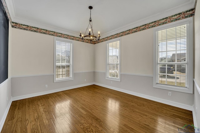 spare room featuring hardwood / wood-style floors, a notable chandelier, a healthy amount of sunlight, and crown molding