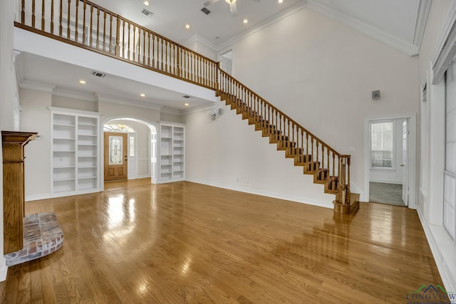 unfurnished living room featuring a high ceiling, built in features, and crown molding