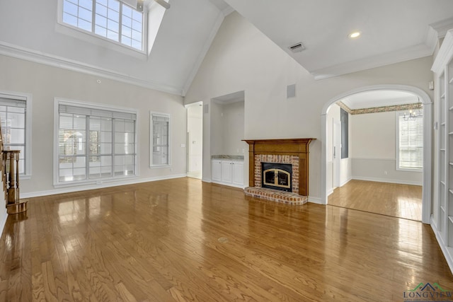 unfurnished living room with light wood-type flooring, a towering ceiling, a brick fireplace, crown molding, and built in features