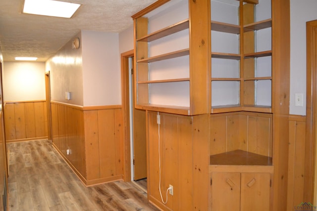 corridor featuring light hardwood / wood-style floors, a textured ceiling, and wood walls