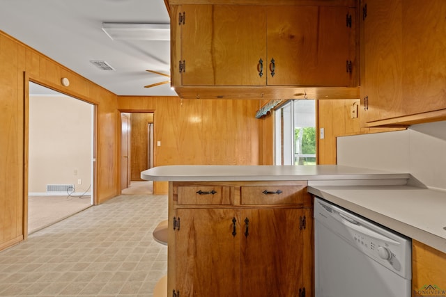 kitchen featuring visible vents, a peninsula, white dishwasher, wooden walls, and light countertops