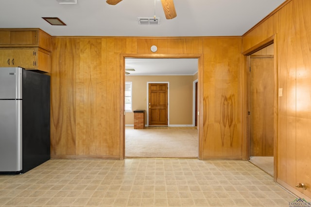 kitchen with wooden walls, ceiling fan, freestanding refrigerator, light floors, and visible vents