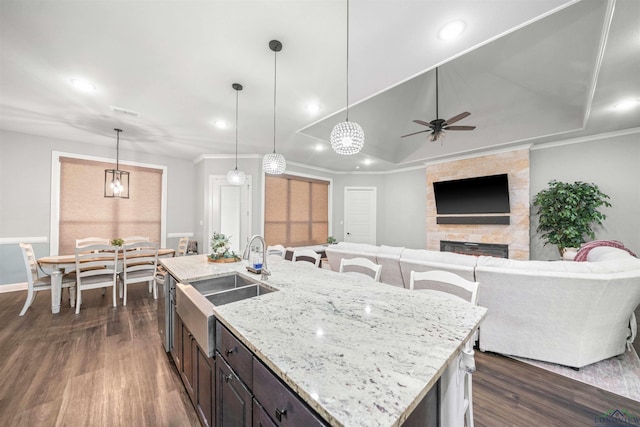 kitchen featuring a sink, open floor plan, hanging light fixtures, a center island with sink, and a stone fireplace