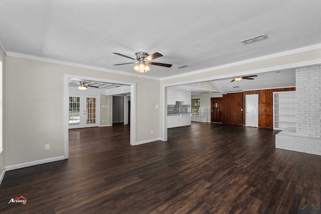 unfurnished living room with dark hardwood / wood-style flooring, ornamental molding, wooden walls, and french doors