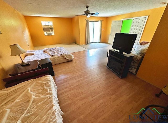 living room with ceiling fan, light wood-type flooring, and a textured ceiling